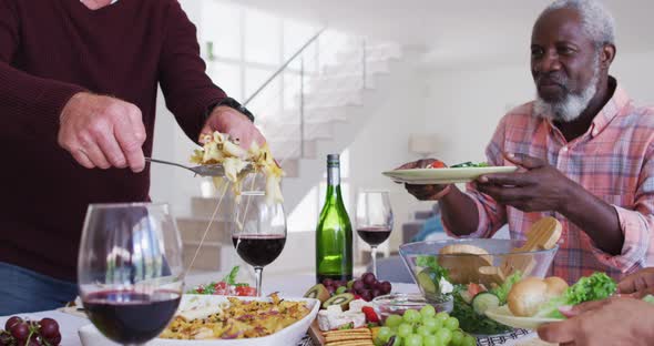 Diverse senior couples sitting by a table drinking wine and eating dinner