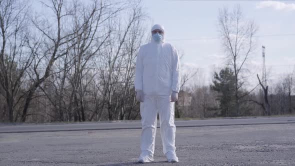 Wide Shot of Caucasian Man in Protective Costume Standing on the Road. Portrait of Young Virologist