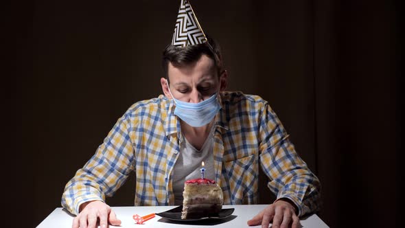 Guy in Face Mask and Coloured Birthday Hat Blows on Candle
