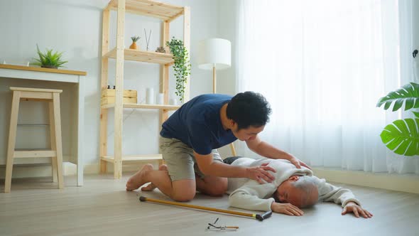 Asian young son helping senior male from falling on the ground at home.