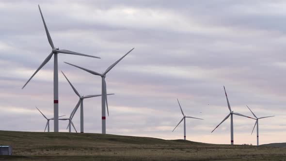 Motion the Blades of a Large Wind Turbine in a Field Against a Background of Orange Sunset on the