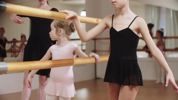 Little Modest Ballerina Girls Training in the Studio Near the Stand with Their Female Trainer