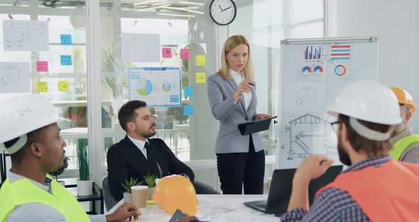 Female Manager Giving Work Instructions to Professional Diverse Team of Builders During meeting