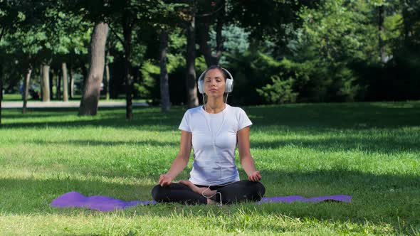 Girl Doing Yoga in the Park and Listening Music on Headphones