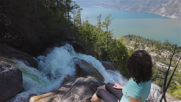 Adventurous Adult Woman is Sitting on Top of a Beautiful Waterfall