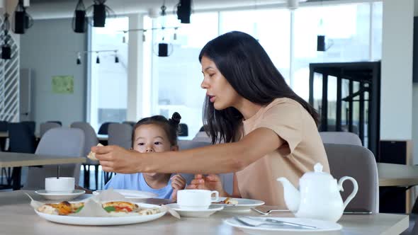 Lady Mom Holds Pizza Slice and Daughter Eats in Cafe