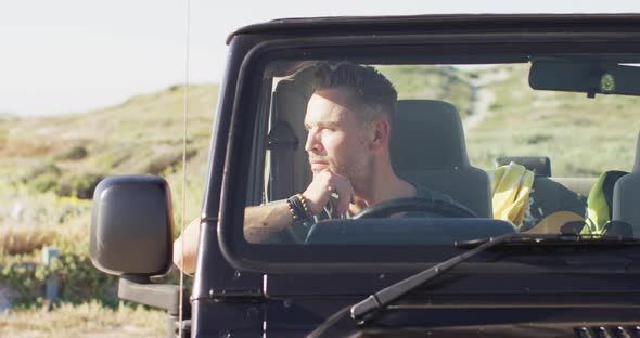 Thoughtful caucasian man sitting in car looking away on sunny day at the beach