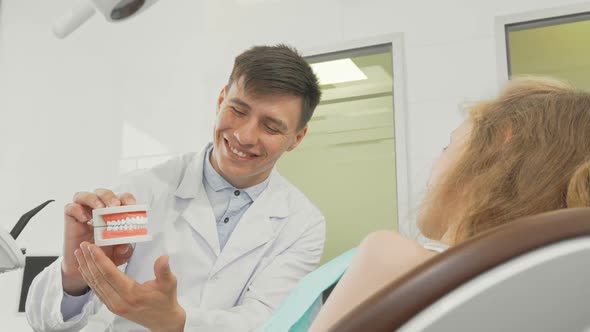 Little Girl Smiling To the Camera Dentist Holding Teeth Model on Back