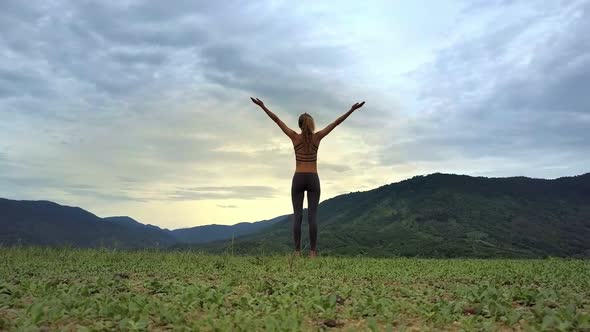 Drone View Girl Stands in Yoga Pose Against Hilly Landscape