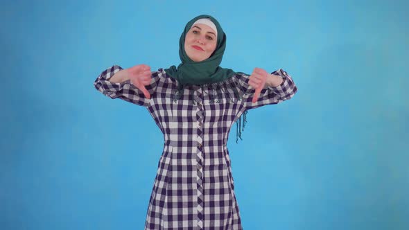 Young Muslim Woman Showing Thumb Down on Blue Background alt