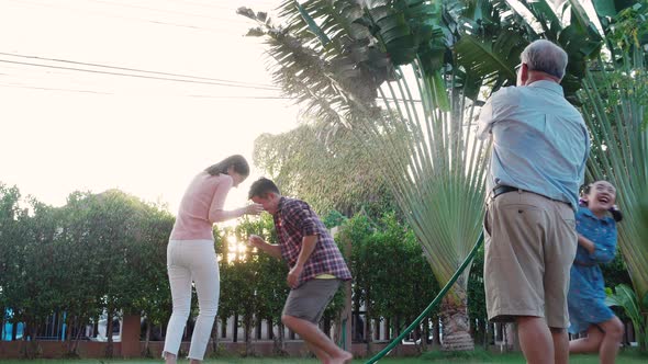 Happy Family playing together during Retired Grandfather watering the plants at the home garden.