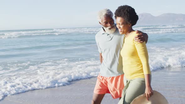Happy african american couple walking and talking on sunny beach