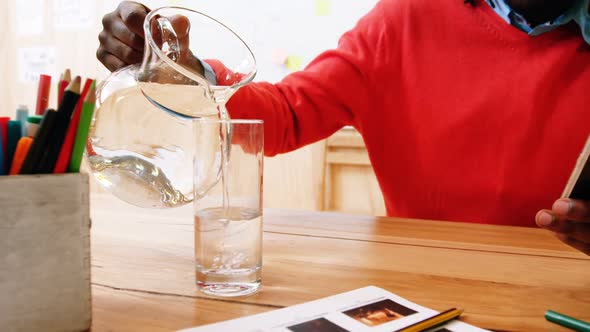 Man pouring jug of water in glass while using mobile phone