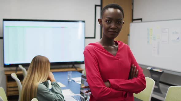 Portrait of african american businesswoman smiling in office, with colleague working in background