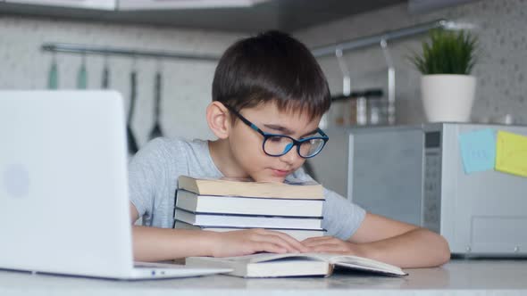 A Schoolboy Does Homework While Sitting in the Kitchen at the Desk Using Many Textbooks. Portrait of