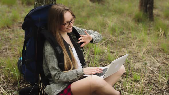 Young Caucasian Girl with Glasses and Backpack Resting in the Nature and Having a Video Call on a