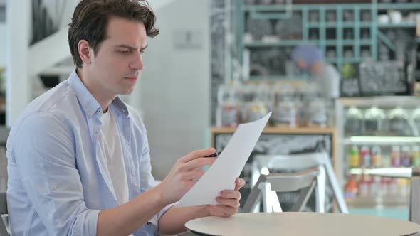 Young Man Reading Documents in Cafe