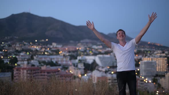 Young Happy Tourist Man Relaxing With Arms Raised On Top Of The Hill At Night