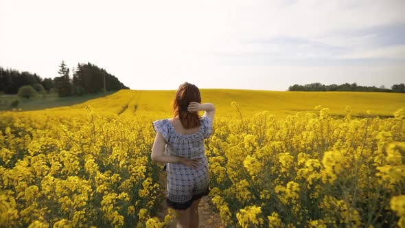 Follow Backside View: Tricky Woman Walks in Rapeseed Field and Turns Around