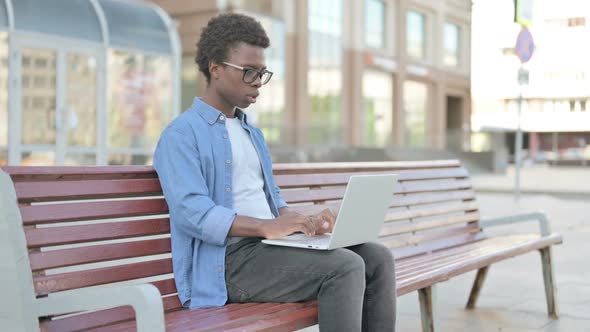 Young African Man Reacting to Loss on Laptop While Sitting Outdoor on Bench