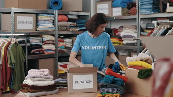 Caucasian Female Volunteer Sorting Clothes and Putting It Into the Cupboard Box at the Warehouse