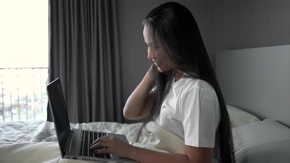 Young woman sitting on bed using laptop for work in bedroom at home