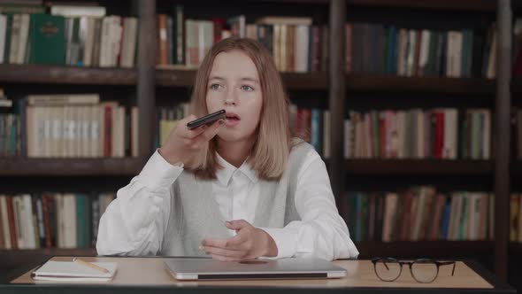 Smiling Female Blonde Child with Short Hair Well Dressed Using Cellphone in School Library Chatting