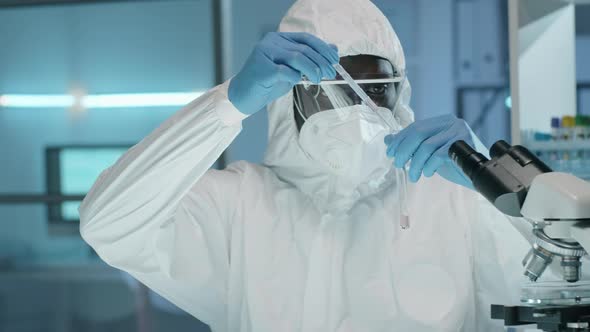 Afro-American Lab Worker in Protective Suit Doing Chemical Experiment