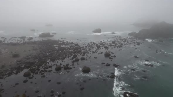 AERIAL: Drone shot descending towards a rocky fog filled coastline.