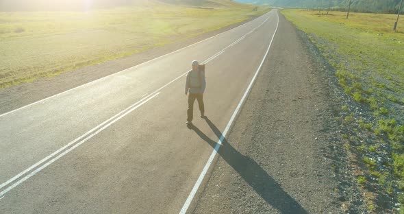 Flight Over Hitchhiker Tourist Walking on Asphalt Road. Huge Rural Valley at Summer Day