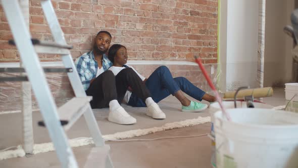 African Couple Sitting on Floor in Empty Room of New Home Planning Design