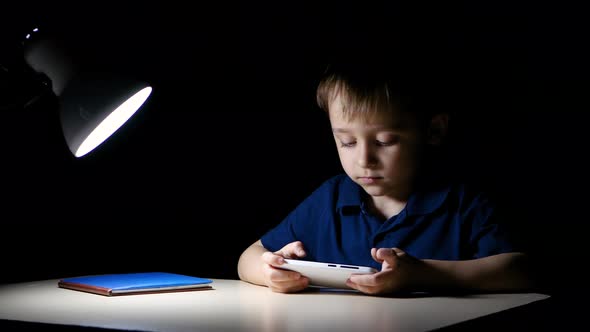 A Child Happily Watches a Cartoon at Home at Night Using a Smartphone