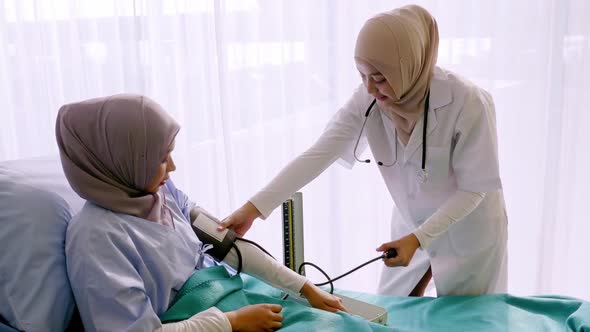 Doctor measuring blood pressure of young woman patient in hospital ward