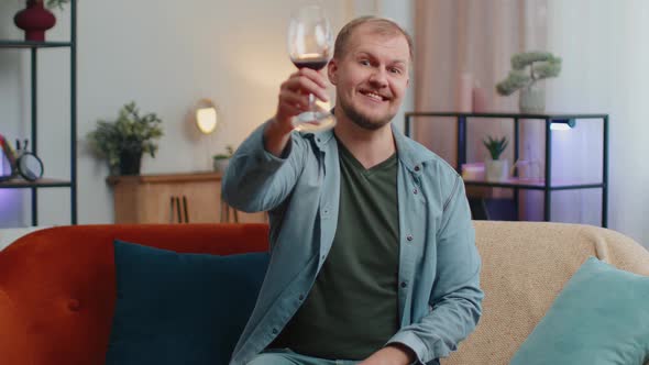 Happy Young Adult Man Drinking Red Wine Glass Celebrating Birthday Anniversary Lottery Win at Home