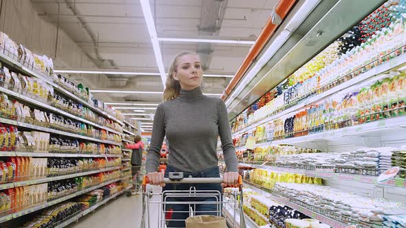 Young Female Walks Between the Shelves in a Grocery Store Visiting a Supermarket a Woman Walks with