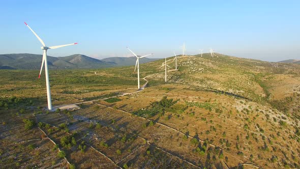 Flying above a group of white wind turbines with red tip blades on a sunny day alt