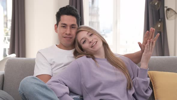 Portrait of young couple smiling and looking at the camera while sitting on the couch at home.