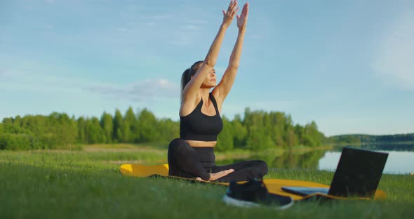 Beautiful Healthy Woman Does Yoga Exercises Using Laptop in the Fresh Air