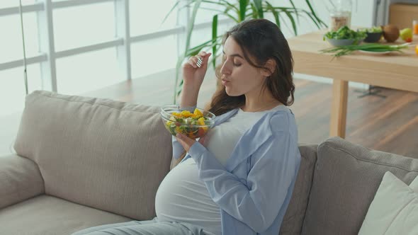 Pregnant Woman With Great Pleasure Eating Vegetable Salad on the Couch