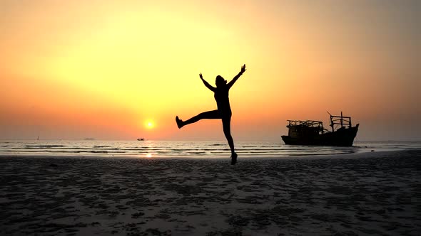 Silhouette of a Girl Joyfully Jumping at Sunset on the Ocean Near To the Ship