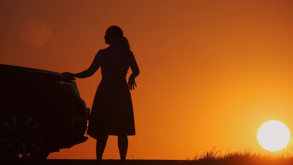 Silhouette of upset woman near broken car in evening on country deserted road