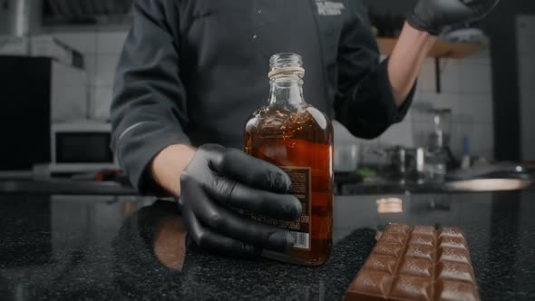 Zooming Shot: Chef in Black Apron and Gloves Opens the Bottle of Cognac and Bung Flies Away in Slow
