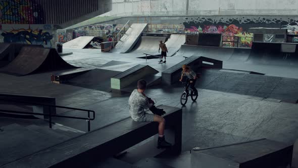 Young Teens Practicing Together on Bmx Bike and Skate Board at Skate Park