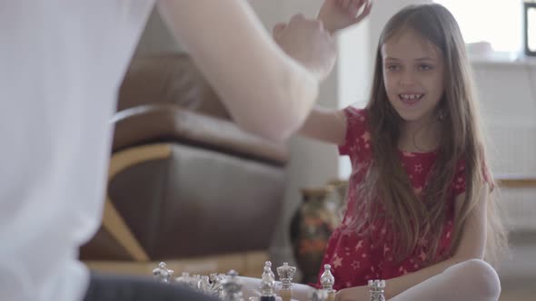 Portrait Unrecognizable Father and Little Girl Playing Chess Sitting on the Floor Close Up. The