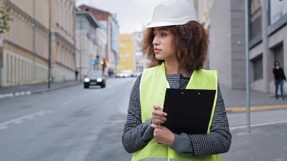 African American Female Engineer in Safety Vest Helmet Hardhat Engineer Standing in City Checking