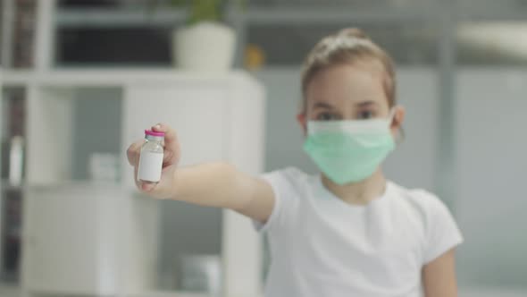 A Pretty Girl in a Mask Holds a Bottle of Medicine in Her Outstretched Hand Against the Background