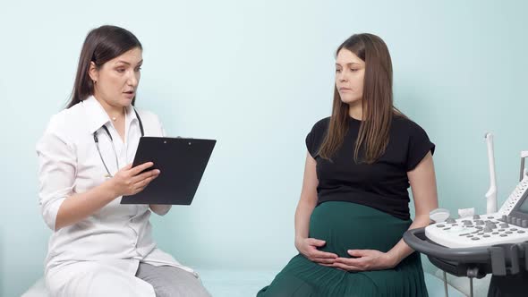 Gynecologist with Clipboard Examines Pregnant Lady in Office