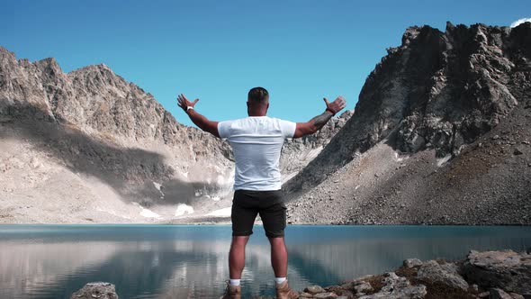 A young man with a beard and an athletic body stands on the top of a mountain