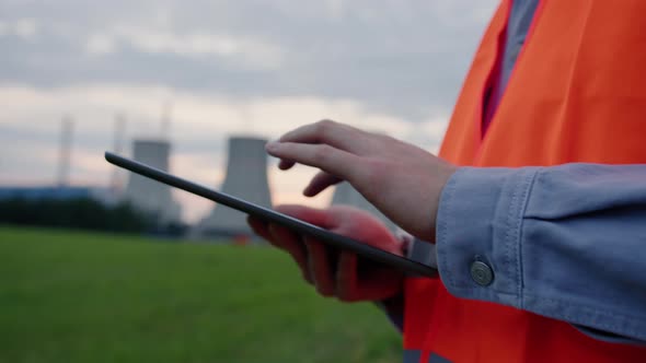 Closeup of a Tablet in the Hands of an Engineer Against the Background of a Power Plant