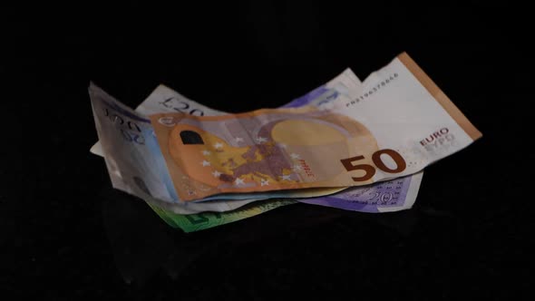 Different banknotes with a 50 euro on top falls in slow motion on a black surface.